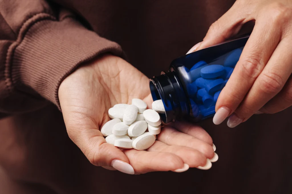 Close-up of a hand pouring white pills from a blue bottle into another person's open hand.